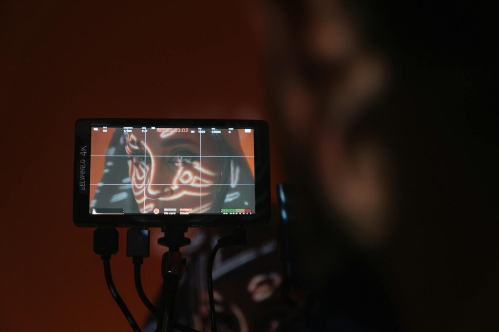 Image of a woman's face with artistic projections captured on a monitor in a dimly-lit setting.