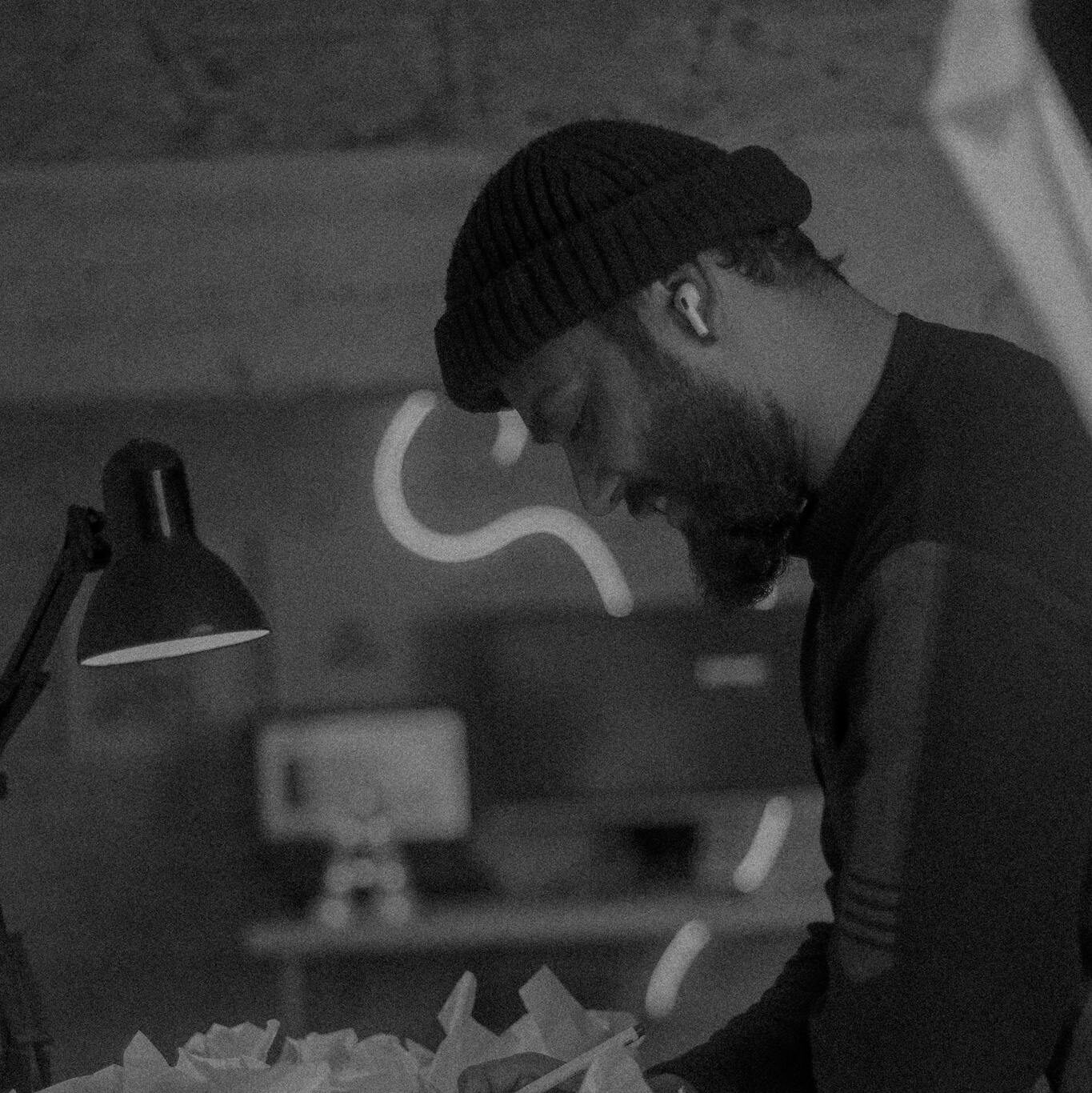 Black and white photo of a man writing in a dimly lit workspace with crumpled paper.